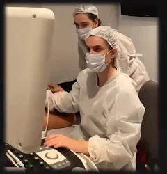 Duas profissionais de máscara e touca operando o aparelho de ultrassom durante o procedimento