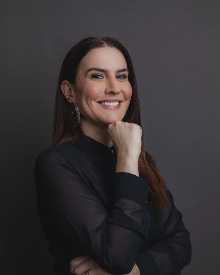 Dra. Fernanda Cavallieri sorrindo, de preto, em retrato de estudio sobre fundo escuro