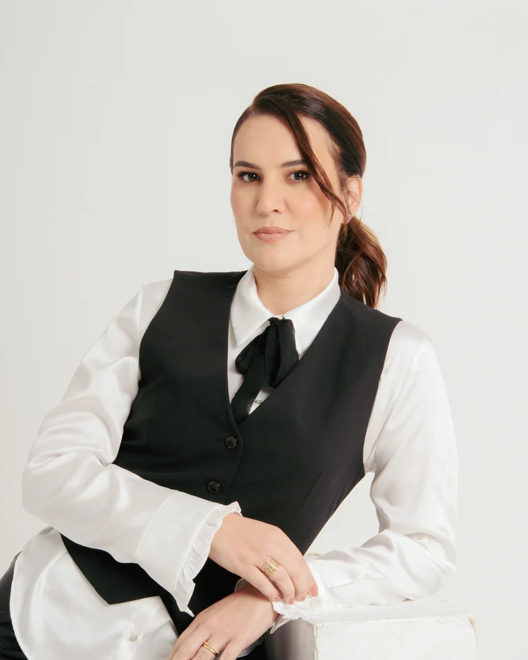 Dra. Fernanda Cavallieri sentada, de colete preto sobre camisa branca e gravata, em retrato de estudio