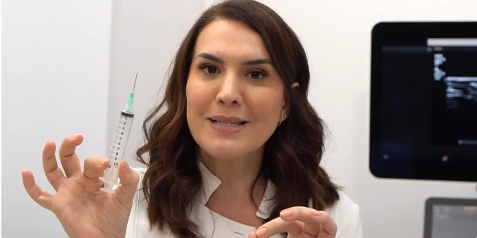 Dra. Fernanda Cavallieri no consultório, com a seringa na mão e o aparelho de ultrassom ao fundo